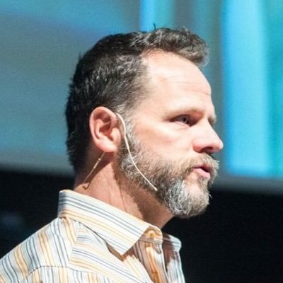 Profile photo of Derek speaking at a conference, wearing a discreet over the ear microphone